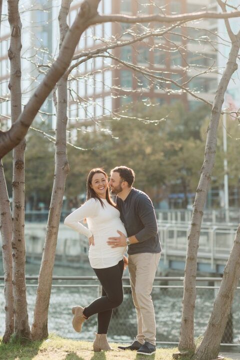 Very hot & sunny afternoon in November I met with Sam and Nick for the maternity session. This expecting parents brought their two fur babies out with them in the hopes of getting some photos of just four before the baby comes next months. Their puppies Cats and Cabo are shih-poos (shih Tzu and Toy Poodle mix) and are too adorable. With Case, Cabo walking along their parents sides we walked along the waterfront of Hoboken NJ. Sam was literally glowing like a porcelain doll and Nick looked so excited and a bit nervous for boy’s arrival. Sam and Nick’s maternity/family session in Hoboken NJ photographed by Karis from Hey Karis. Photograph is like freezing time, motion in print, movie turned into a book. Now booking 2021 and 2022 weddings.