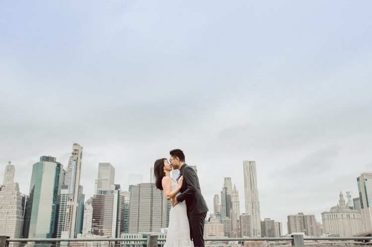 DUMBO Brooklyn NY photographing Stella and Peter's engagement. Temperature dropped dramatically, sky was covered in cloud and was windy but you can't possibly tell by Stella's chic outfit, white strap dress with white kitten heel mules and Peter in his suit and a Gucci tie. Per their outfits, my concept for Stella and Peter's engagement session geared to more editorial. As I shoot I tried to imagine a story in which I want to create and tell through my photos in every session. Stella and Peter's DUMBO Brooklyn Engagement Session captured by NY NJ Documentary Wedding Photographer Karis from Hey Karis, photographing your wedding moments cinematically.