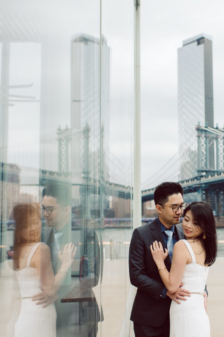 DUMBO Brooklyn NY photographing Stella and Peter's engagement. Temperature dropped dramatically, sky was covered in cloud and was windy but you can't possibly tell by Stella's chic outfit, white strap dress with white kitten heel mules and Peter in his suit and a Gucci tie. Per their outfits, my concept for Stella and Peter's engagement session geared to more editorial. As I shoot I tried to imagine a story in which I want to create and tell through my photos in every session. Stella and Peter's DUMBO Brooklyn Engagement Session captured by NY NJ Documentary Wedding Photographer Karis from Hey Karis, photographing your wedding moments cinematically.