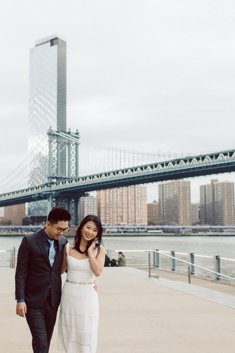 DUMBO Brooklyn NY photographing Stella and Peter's engagement. Temperature dropped dramatically, sky was covered in cloud and was windy but you can't possibly tell by Stella's chic outfit, white strap dress with white kitten heel mules and Peter in his suit and a Gucci tie. Per their outfits, my concept for Stella and Peter's engagement session geared to more editorial. As I shoot I tried to imagine a story in which I want to create and tell through my photos in every session. Stella and Peter's DUMBO Brooklyn Engagement Session captured by NY NJ Documentary Wedding Photographer Karis from Hey Karis, photographing your wedding moments cinematically.