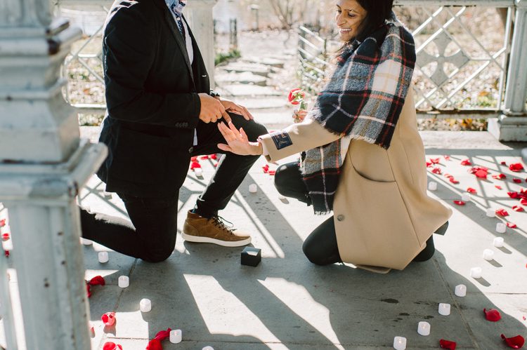 Nisha and Sagar's Ladies Pavilion Central Park NY proposal on a sunny sunday afternoon went just as Sagar planned it to be and more with their friends to celebrate together. Nisha and Sagar walked from their NYC apartment to Ladies Pavilion Central Park pretending to meet their friends for a pop up lunch but as soon as Nisha saw all her girlfriends standing by Ladies Pavilion holding roses, she quickly figured out what was about to happen. Then Sagar walked Nisha over into Ladies Pavilion where it was decorated with candles and rose pedals, Sagar went down on his one knee pulled out the ring. Watching Sagar go on his knee Nisha also went on her knee and received her ring while saying "Yes" and hugging him. All the emotions, tears hanging off her big round eyes. I truly felt so honored to be able to capture this special moment in their lives for them, documenting the beginning of their next chapter in life. Nisha and Sagar's Ladies Pavilion Central Park proposal captured by NY NJ Documentary Wedding Photographer Karis from Hey Karis, photographing your wedding, capturing your love and documenting your life.