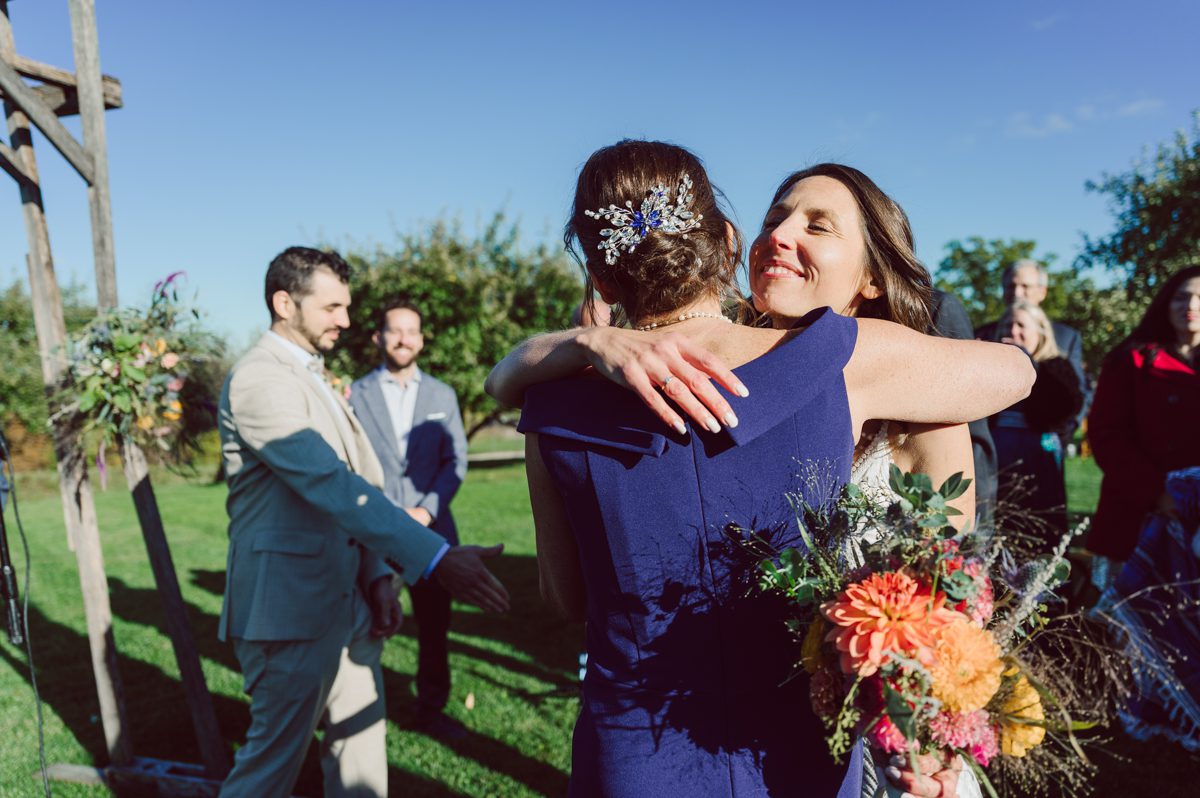 Talking about climate change (global warming) we've been having weirdly warm almost hot Fall. So we were hoping so another warm day for Becca and Dan's wedding on October 8, 2022 but unfortunately non of us were that lucky and it was pretty chilly. Especially at The Farm at Glenwood Mountain NJ which is pretty Northern NJ it felt or was colder, windier and just chillier. Thankfully I brought the right jacket for the chilly wind on the top of Glenwood Mountain but OMG I felt so bad for my bride Becca only wearing her lace wedding dress standing outside on top of Glenwood Mountain during the wedding ceremony. But before I talk about the wedding ceremony let's start from Becca and Dan's wedding prep which took place onsite at The Farm at Glenwood Mountain in Sussex NJ. Becca got ready cozy in the bridal suit when Dan just got ready by the Barn at The Farm at Glenwood Mountain and we went straight into Becca and Dan's first look next to the Highland Cows! Cutest fluffy Highland Cows were all out by the field and chilled while we took some wedding portraits of Becca and Dan. One of the many reasons "I LOVE" this wedding venue "The Farm at Glenwood Mountain" is because of these adorable Fluffy Cows called Highland Cows! I can stare at the all day long and take photo of them all day long. After Becca and Dan's first look, wedding portraits and family photos were done I walked up to the hill to Becca and Dan's outdoor ceremony area on top of the hill at The Farm at Glenwood Mountain and along the way I saw more cute baby Highland Cows to photograph and stare and wave hello. Watched guests arrive in a Yellow School bus in any rustic Farm wedding style and was them walk up the hill. Following the path, the fence with The Barn at their backdrop. Sun was out, it was clear gorgeous day but bit chilly and definitely way windy on top of the hill. My groom Dan came up along with their dog Dash (Dasher), then finally Becca arrived with her parents along side her. Ceremony started quickly knowing that guests and bride probably are freezing, Wind kept moving the cloud in and out making me change my exposure non stop. Wind blew hard, moving Becca's hair all over the place. But non the less it was sincere and beautiful wedding ceremony surrounded by nature, trees and Highland Cows Becca and Dan said their wedding vows followed by I do's. Sealing the wedding ceremony with a kiss Becca and Dan walked down the aisle quickly as possible to bundle Becca in to something warm. Amazing food, spread and hors d'oeuvres were passed out and when the sun was setting everyone made their way in to the barn for warmth and to seated for Becca and Dan's wedding reception. Gorgeous structured barn at The Farm at Glenwood Mountain is definitely not your typical too rustic and broken down barn, the barn here is new, clean, architectural and gorgeous! The owner Chef Steve even makes everyone take off their shoes if we need to enter the barn before the reception. Just like that Becca and Dan danced and partied their way into the night and it was already time for their barn fire and s'mores time outside. Becca and Dan's The Farm at Glenwood Mountain Sussex NJ wedding captured by Karis from Hey Karis New York, Brooklyn, Hudson Valley and Catskills Wedding Photographer and NYC Elopement Photographer.
