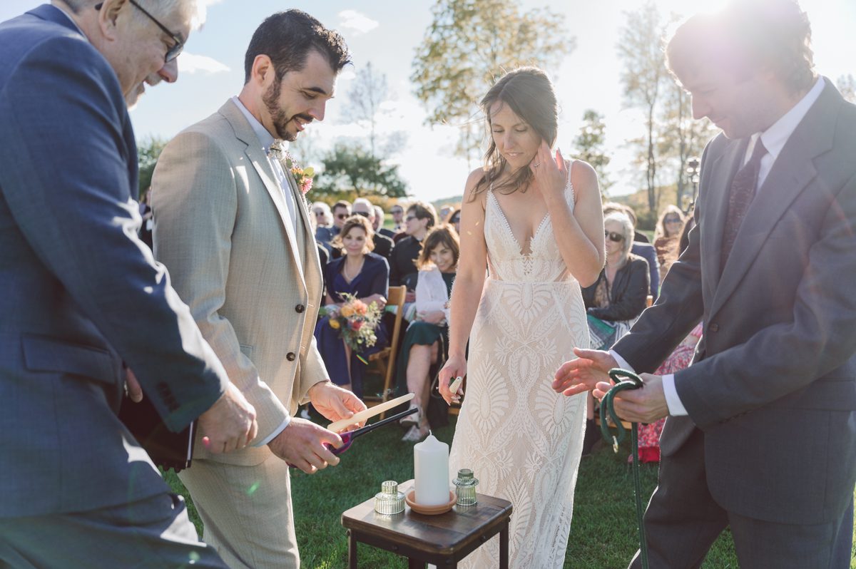 Talking about climate change (global warming) we've been having weirdly warm almost hot Fall. So we were hoping so another warm day for Becca and Dan's wedding on October 8, 2022 but unfortunately non of us were that lucky and it was pretty chilly. Especially at The Farm at Glenwood Mountain NJ which is pretty Northern NJ it felt or was colder, windier and just chillier. Thankfully I brought the right jacket for the chilly wind on the top of Glenwood Mountain but OMG I felt so bad for my bride Becca only wearing her lace wedding dress standing outside on top of Glenwood Mountain during the wedding ceremony. But before I talk about the wedding ceremony let's start from Becca and Dan's wedding prep which took place onsite at The Farm at Glenwood Mountain in Sussex NJ. Becca got ready cozy in the bridal suit when Dan just got ready by the Barn at The Farm at Glenwood Mountain and we went straight into Becca and Dan's first look next to the Highland Cows! Cutest fluffy Highland Cows were all out by the field and chilled while we took some wedding portraits of Becca and Dan. One of the many reasons "I LOVE" this wedding venue "The Farm at Glenwood Mountain" is because of these adorable Fluffy Cows called Highland Cows! I can stare at the all day long and take photo of them all day long. After Becca and Dan's first look, wedding portraits and family photos were done I walked up to the hill to Becca and Dan's outdoor ceremony area on top of the hill at The Farm at Glenwood Mountain and along the way I saw more cute baby Highland Cows to photograph and stare and wave hello. Watched guests arrive in a Yellow School bus in any rustic Farm wedding style and was them walk up the hill. Following the path, the fence with The Barn at their backdrop. Sun was out, it was clear gorgeous day but bit chilly and definitely way windy on top of the hill. My groom Dan came up along with their dog Dash (Dasher), then finally Becca arrived with her parents along side her. Ceremony started quickly knowing that guests and bride probably are freezing, Wind kept moving the cloud in and out making me change my exposure non stop. Wind blew hard, moving Becca's hair all over the place. But non the less it was sincere and beautiful wedding ceremony surrounded by nature, trees and Highland Cows Becca and Dan said their wedding vows followed by I do's. Sealing the wedding ceremony with a kiss Becca and Dan walked down the aisle quickly as possible to bundle Becca in to something warm. Amazing food, spread and hors d'oeuvres were passed out and when the sun was setting everyone made their way in to the barn for warmth and to seated for Becca and Dan's wedding reception. Gorgeous structured barn at The Farm at Glenwood Mountain is definitely not your typical too rustic and broken down barn, the barn here is new, clean, architectural and gorgeous! The owner Chef Steve even makes everyone take off their shoes if we need to enter the barn before the reception. Just like that Becca and Dan danced and partied their way into the night and it was already time for their barn fire and s'mores time outside. Becca and Dan's The Farm at Glenwood Mountain Sussex NJ wedding captured by Karis from Hey Karis New York, Brooklyn, Hudson Valley and Catskills Wedding Photographer and NYC Elopement Photographer.
