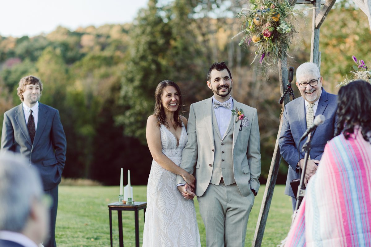 Talking about climate change (global warming) we've been having weirdly warm almost hot Fall. So we were hoping so another warm day for Becca and Dan's wedding on October 8, 2022 but unfortunately non of us were that lucky and it was pretty chilly. Especially at The Farm at Glenwood Mountain NJ which is pretty Northern NJ it felt or was colder, windier and just chillier. Thankfully I brought the right jacket for the chilly wind on the top of Glenwood Mountain but OMG I felt so bad for my bride Becca only wearing her lace wedding dress standing outside on top of Glenwood Mountain during the wedding ceremony. But before I talk about the wedding ceremony let's start from Becca and Dan's wedding prep which took place onsite at The Farm at Glenwood Mountain in Sussex NJ. Becca got ready cozy in the bridal suit when Dan just got ready by the Barn at The Farm at Glenwood Mountain and we went straight into Becca and Dan's first look next to the Highland Cows! Cutest fluffy Highland Cows were all out by the field and chilled while we took some wedding portraits of Becca and Dan. One of the many reasons "I LOVE" this wedding venue "The Farm at Glenwood Mountain" is because of these adorable Fluffy Cows called Highland Cows! I can stare at the all day long and take photo of them all day long. After Becca and Dan's first look, wedding portraits and family photos were done I walked up to the hill to Becca and Dan's outdoor ceremony area on top of the hill at The Farm at Glenwood Mountain and along the way I saw more cute baby Highland Cows to photograph and stare and wave hello. Watched guests arrive in a Yellow School bus in any rustic Farm wedding style and was them walk up the hill. Following the path, the fence with The Barn at their backdrop. Sun was out, it was clear gorgeous day but bit chilly and definitely way windy on top of the hill. My groom Dan came up along with their dog Dash (Dasher), then finally Becca arrived with her parents along side her. Ceremony started quickly knowing that guests and bride probably are freezing, Wind kept moving the cloud in and out making me change my exposure non stop. Wind blew hard, moving Becca's hair all over the place. But non the less it was sincere and beautiful wedding ceremony surrounded by nature, trees and Highland Cows Becca and Dan said their wedding vows followed by I do's. Sealing the wedding ceremony with a kiss Becca and Dan walked down the aisle quickly as possible to bundle Becca in to something warm. Amazing food, spread and hors d'oeuvres were passed out and when the sun was setting everyone made their way in to the barn for warmth and to seated for Becca and Dan's wedding reception. Gorgeous structured barn at The Farm at Glenwood Mountain is definitely not your typical too rustic and broken down barn, the barn here is new, clean, architectural and gorgeous! The owner Chef Steve even makes everyone take off their shoes if we need to enter the barn before the reception. Just like that Becca and Dan danced and partied their way into the night and it was already time for their barn fire and s'mores time outside. Becca and Dan's The Farm at Glenwood Mountain Sussex NJ wedding captured by Karis from Hey Karis New York, Brooklyn, Hudson Valley and Catskills Wedding Photographer and NYC Elopement Photographer.
