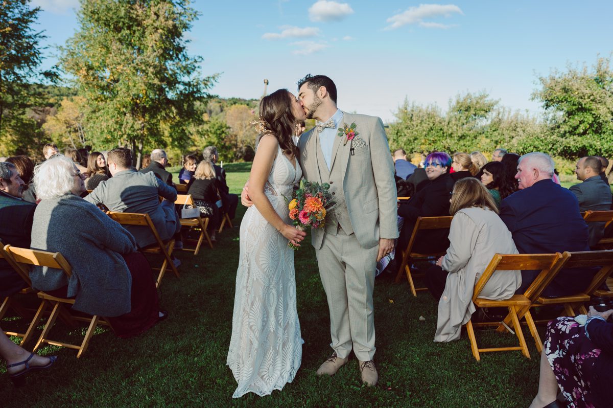 Talking about climate change (global warming) we've been having weirdly warm almost hot Fall. So we were hoping so another warm day for Becca and Dan's wedding on October 8, 2022 but unfortunately non of us were that lucky and it was pretty chilly. Especially at The Farm at Glenwood Mountain NJ which is pretty Northern NJ it felt or was colder, windier and just chillier. Thankfully I brought the right jacket for the chilly wind on the top of Glenwood Mountain but OMG I felt so bad for my bride Becca only wearing her lace wedding dress standing outside on top of Glenwood Mountain during the wedding ceremony. But before I talk about the wedding ceremony let's start from Becca and Dan's wedding prep which took place onsite at The Farm at Glenwood Mountain in Sussex NJ. Becca got ready cozy in the bridal suit when Dan just got ready by the Barn at The Farm at Glenwood Mountain and we went straight into Becca and Dan's first look next to the Highland Cows! Cutest fluffy Highland Cows were all out by the field and chilled while we took some wedding portraits of Becca and Dan. One of the many reasons "I LOVE" this wedding venue "The Farm at Glenwood Mountain" is because of these adorable Fluffy Cows called Highland Cows! I can stare at the all day long and take photo of them all day long. After Becca and Dan's first look, wedding portraits and family photos were done I walked up to the hill to Becca and Dan's outdoor ceremony area on top of the hill at The Farm at Glenwood Mountain and along the way I saw more cute baby Highland Cows to photograph and stare and wave hello. Watched guests arrive in a Yellow School bus in any rustic Farm wedding style and was them walk up the hill. Following the path, the fence with The Barn at their backdrop. Sun was out, it was clear gorgeous day but bit chilly and definitely way windy on top of the hill. My groom Dan came up along with their dog Dash (Dasher), then finally Becca arrived with her parents along side her. Ceremony started quickly knowing that guests and bride probably are freezing, Wind kept moving the cloud in and out making me change my exposure non stop. Wind blew hard, moving Becca's hair all over the place. But non the less it was sincere and beautiful wedding ceremony surrounded by nature, trees and Highland Cows Becca and Dan said their wedding vows followed by I do's. Sealing the wedding ceremony with a kiss Becca and Dan walked down the aisle quickly as possible to bundle Becca in to something warm. Amazing food, spread and hors d'oeuvres were passed out and when the sun was setting everyone made their way in to the barn for warmth and to seated for Becca and Dan's wedding reception. Gorgeous structured barn at The Farm at Glenwood Mountain is definitely not your typical too rustic and broken down barn, the barn here is new, clean, architectural and gorgeous! The owner Chef Steve even makes everyone take off their shoes if we need to enter the barn before the reception. Just like that Becca and Dan danced and partied their way into the night and it was already time for their barn fire and s'mores time outside. Becca and Dan's The Farm at Glenwood Mountain Sussex NJ wedding captured by Karis from Hey Karis New York, Brooklyn, Hudson Valley and Catskills Wedding Photographer and NYC Elopement Photographer.
