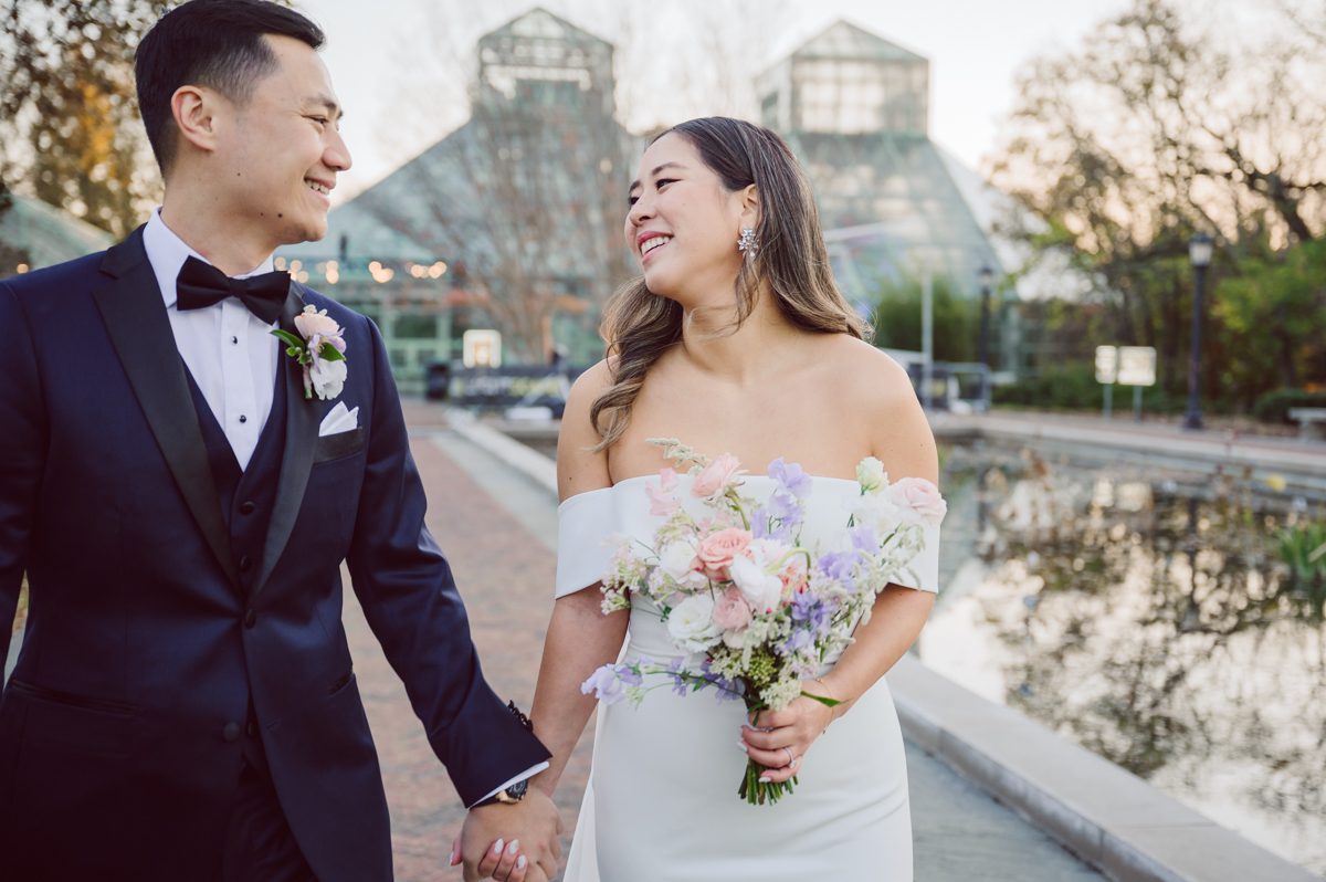 Duffield St, Brooklyn on November 19 even though it's Saturday morning it was still very busy. But luckily I found street parking right on Duffield St in front of Sheraton Downtown Brooklyn which was where I needed to be for Ariana and Jon's wedding prep. Vicky from VickyC5 hair/makeup team was there beautifying the ladies, I went straight to flat lays of Ariana's wedding details such as rings, jewelry and her wedding invitations. I use ribbons, extra loose flowers to make the flat lays more fine art looking. Once all the details are done, my full focus goes to the bride Ariana and her ladies. Ariana and Jon were planning to do a Chinese Door Game at the hotel room, so as soon as Ariana was ready in her Hanbok (Korean Traditional Wedding Outfit) Jon and his groomsmen arrived at the door. With Ariana's bridal suite crowded with too many people Ariana's bridesmaids started to give instructions to the games that Jon and his groomsmen need to play in order to get through the second door so that Jon can meet/see his bride Ariana. While the games are happening outside Ariana's door one of the bridesmaid has her phone on FaceTime so that Ariana can see how the men are doing during all the door games. I of course had my second shooter inside the room with Ariana to get her reactions which was hilarious. After the door games, we then moved to a conference room of at Sheraton Downtown Brooklyn for Ariana and Jon's Chinese Tea Pouring Ceremony (this is Jon's Chinese side's wedding tradition where you pour tea to all the elders in the family). Once all the Chines and Korean wedding traditions are over, we all rushed to Brooklyn Botanical Garden. Traffic from Sheraton Downtown Brooklyn to Brooklyn Botanical Garden was pretty bad, as usual. Once I arrived there of course was no street parking available near the entrance and parking lot for Brooklyn Botanical Garden was way too far for me to carry all the gears. After driving around I found one spot few blocks away from the Brooklyn Botanical Garden entrance. Brooklyn Botanical Garden was busy with Lightscape preparation and installation which we were not allowed to photograph so we were left with very little options for wedding portrait backdrop, plus it was COLD and we were looking light! These are important things to consider when you are planning for Winter wedding. I worked as quickly as possible with Ariana and Jon's first look and bridal party photos. Then we stayed inside for family photos since elders did not wanted to go outside which I totally don't blame. Then I quickly took Ariana and Jon outside for bit more couple's portraits then it was time for the wedding ceremony. Ariana and Jon's wedding ceremony held place at The Palm House at Brooklyn Botanical Garden, but because it was an winter wedding we've lost all the light and I had to use my video lights but over all the ceremony was beautiful and Oh Fleur NYC did absolutely an amazing job with ceremony decor (floral/candles). The Palm House was empty again, OhfleurNYC as well as Brooklyn Botanical Garden staff were busy turning the room. Oh Fleur NYC's Jessica's talent was amazing her usage of floral, choice of colors and mixing the floral with tall candles were magical. Turned The Palm House into a beautiful and romantic garden. Warmth of candles, peach and pinks of flowers all blended so well turning the Palm House at Brooklyn Botanical Garden in to fairytale floral ballroom. Ariana and Jon attended cocktail enjoying their time with friends and family before their wedding reception at The Palm House. Ariana and Jon's wedding at The Palm House at Brooklyn Botanical Garden documented by Karis from Hey Karis New York, Brooklyn, Hudson Valley and Catskills Wedding Photographer and NYC Elopement Photographer.