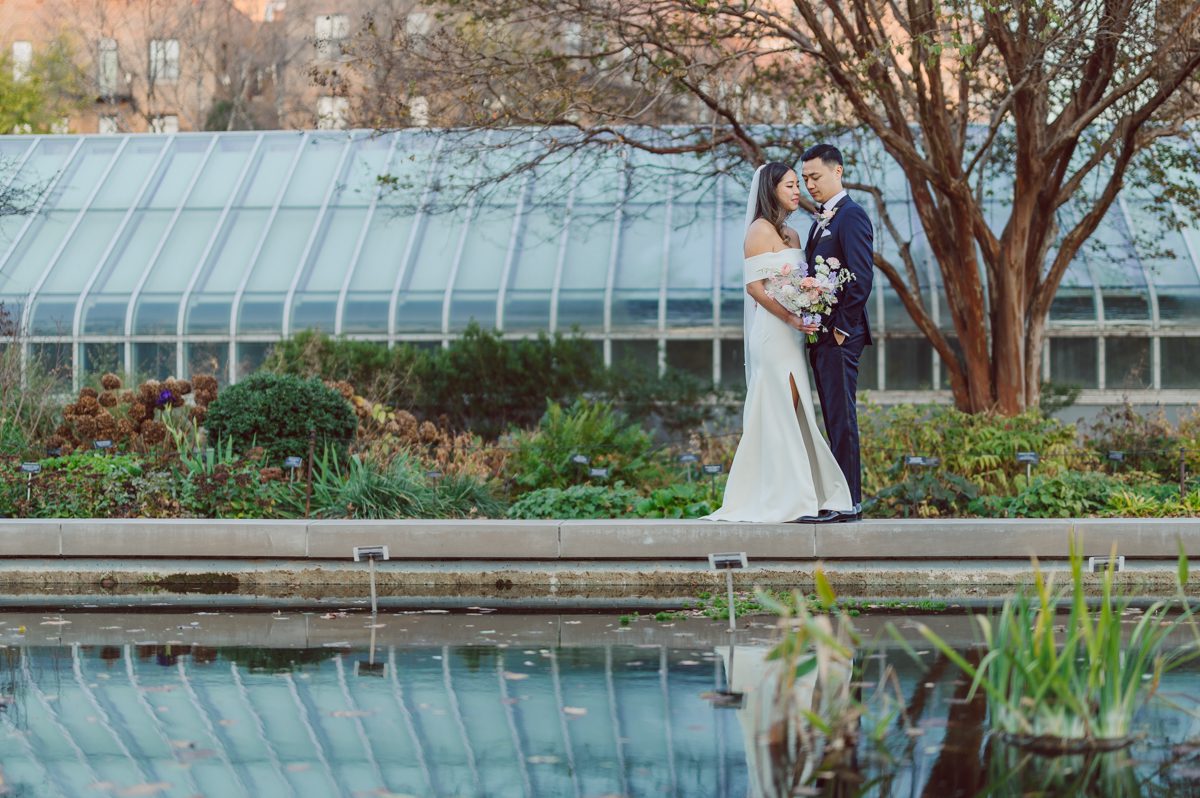 Duffield St, Brooklyn on November 19 even though it's Saturday morning it was still very busy. But luckily I found street parking right on Duffield St in front of Sheraton Downtown Brooklyn which was where I needed to be for Ariana and Jon's wedding prep. Vicky from VickyC5 hair/makeup team was there beautifying the ladies, I went straight to flat lays of Ariana's wedding details such as rings, jewelry and her wedding invitations. I use ribbons, extra loose flowers to make the flat lays more fine art looking. Once all the details are done, my full focus goes to the bride Ariana and her ladies. Ariana and Jon were planning to do a Chinese Door Game at the hotel room, so as soon as Ariana was ready in her Hanbok (Korean Traditional Wedding Outfit) Jon and his groomsmen arrived at the door. With Ariana's bridal suite crowded with too many people Ariana's bridesmaids started to give instructions to the games that Jon and his groomsmen need to play in order to get through the second door so that Jon can meet/see his bride Ariana. While the games are happening outside Ariana's door one of the bridesmaid has her phone on FaceTime so that Ariana can see how the men are doing during all the door games. I of course had my second shooter inside the room with Ariana to get her reactions which was hilarious. After the door games, we then moved to a conference room of at Sheraton Downtown Brooklyn for Ariana and Jon's Chinese Tea Pouring Ceremony (this is Jon's Chinese side's wedding tradition where you pour tea to all the elders in the family). Once all the Chines and Korean wedding traditions are over, we all rushed to Brooklyn Botanical Garden. Traffic from Sheraton Downtown Brooklyn to Brooklyn Botanical Garden was pretty bad, as usual. Once I arrived there of course was no street parking available near the entrance and parking lot for Brooklyn Botanical Garden was way too far for me to carry all the gears. After driving around I found one spot few blocks away from the Brooklyn Botanical Garden entrance. Brooklyn Botanical Garden was busy with Lightscape preparation and installation which we were not allowed to photograph so we were left with very little options for wedding portrait backdrop, plus it was COLD and we were looking light! These are important things to consider when you are planning for Winter wedding. I worked as quickly as possible with Ariana and Jon's first look and bridal party photos. Then we stayed inside for family photos since elders did not wanted to go outside which I totally don't blame. Then I quickly took Ariana and Jon outside for bit more couple's portraits then it was time for the wedding ceremony. Ariana and Jon's wedding ceremony held place at The Palm House at Brooklyn Botanical Garden, but because it was an winter wedding we've lost all the light and I had to use my video lights but over all the ceremony was beautiful and Oh Fleur NYC did absolutely an amazing job with ceremony decor (floral/candles). The Palm House was empty again, OhfleurNYC as well as Brooklyn Botanical Garden staff were busy turning the room. Oh Fleur NYC's Jessica's talent was amazing her usage of floral, choice of colors and mixing the floral with tall candles were magical. Turned The Palm House into a beautiful and romantic garden. Warmth of candles, peach and pinks of flowers all blended so well turning the Palm House at Brooklyn Botanical Garden in to fairytale floral ballroom. Ariana and Jon attended cocktail enjoying their time with friends and family before their wedding reception at The Palm House. Ariana and Jon's wedding at The Palm House at Brooklyn Botanical Garden documented by Karis from Hey Karis New York, Brooklyn, Hudson Valley and Catskills Wedding Photographer and NYC Elopement Photographer.