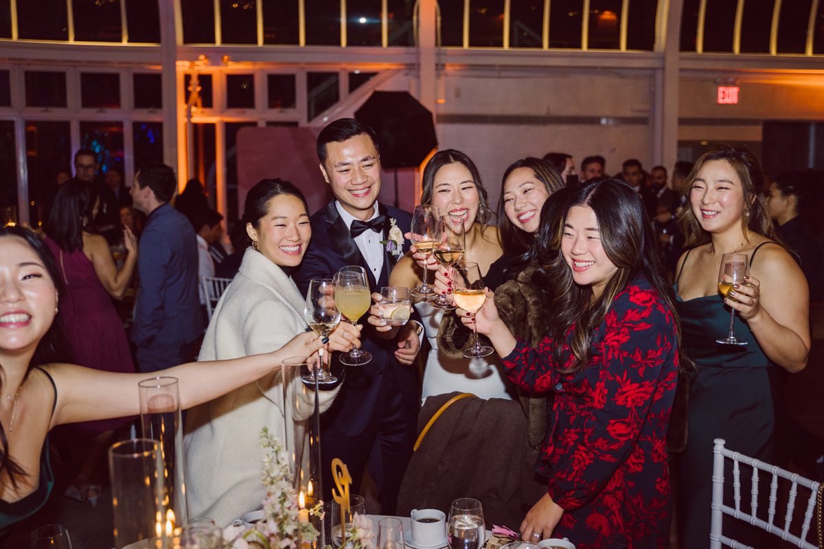 Duffield St, Brooklyn on November 19 even though it's Saturday morning it was still very busy. But luckily I found street parking right on Duffield St in front of Sheraton Downtown Brooklyn which was where I needed to be for Ariana and Jon's wedding prep. Vicky from VickyC5 hair/makeup team was there beautifying the ladies, I went straight to flat lays of Ariana's wedding details such as rings, jewelry and her wedding invitations. I use ribbons, extra loose flowers to make the flat lays more fine art looking. Once all the details are done, my full focus goes to the bride Ariana and her ladies. Ariana and Jon were planning to do a Chinese Door Game at the hotel room, so as soon as Ariana was ready in her Hanbok (Korean Traditional Wedding Outfit) Jon and his groomsmen arrived at the door. With Ariana's bridal suite crowded with too many people Ariana's bridesmaids started to give instructions to the games that Jon and his groomsmen need to play in order to get through the second door so that Jon can meet/see his bride Ariana. While the games are happening outside Ariana's door one of the bridesmaid has her phone on FaceTime so that Ariana can see how the men are doing during all the door games. I of course had my second shooter inside the room with Ariana to get her reactions which was hilarious. After the door games, we then moved to a conference room of at Sheraton Downtown Brooklyn for Ariana and Jon's Chinese Tea Pouring Ceremony (this is Jon's Chinese side's wedding tradition where you pour tea to all the elders in the family). Once all the Chines and Korean wedding traditions are over, we all rushed to Brooklyn Botanical Garden. Traffic from Sheraton Downtown Brooklyn to Brooklyn Botanical Garden was pretty bad, as usual. Once I arrived there of course was no street parking available near the entrance and parking lot for Brooklyn Botanical Garden was way too far for me to carry all the gears. After driving around I found one spot few blocks away from the Brooklyn Botanical Garden entrance. Brooklyn Botanical Garden was busy with Lightscape preparation and installation which we were not allowed to photograph so we were left with very little options for wedding portrait backdrop, plus it was COLD and we were looking light! These are important things to consider when you are planning for Winter wedding. I worked as quickly as possible with Ariana and Jon's first look and bridal party photos. Then we stayed inside for family photos since elders did not wanted to go outside which I totally don't blame. Then I quickly took Ariana and Jon outside for bit more couple's portraits then it was time for the wedding ceremony. Ariana and Jon's wedding ceremony held place at The Palm House at Brooklyn Botanical Garden, but because it was an winter wedding we've lost all the light and I had to use my video lights but over all the ceremony was beautiful and Oh Fleur NYC did absolutely an amazing job with ceremony decor (floral/candles). The Palm House was empty again, OhfleurNYC as well as Brooklyn Botanical Garden staff were busy turning the room. Oh Fleur NYC's Jessica's talent was amazing her usage of floral, choice of colors and mixing the floral with tall candles were magical. Turned The Palm House into a beautiful and romantic garden. Warmth of candles, peach and pinks of flowers all blended so well turning the Palm House at Brooklyn Botanical Garden in to fairytale floral ballroom. Ariana and Jon attended cocktail enjoying their time with friends and family before their wedding reception at The Palm House. Ariana and Jon's wedding at The Palm House at Brooklyn Botanical Garden documented by Karis from Hey Karis New York, Brooklyn, Hudson Valley and Catskills Wedding Photographer and NYC Elopement Photographer.