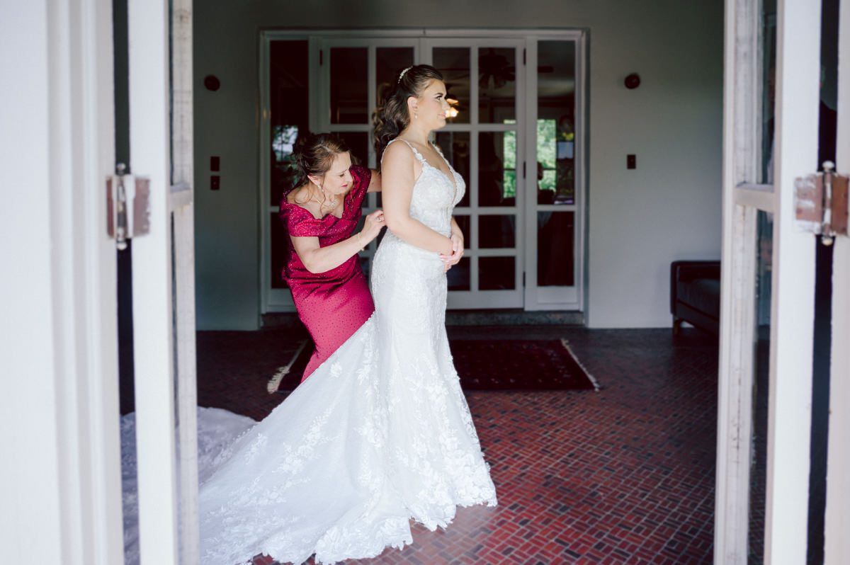 How do I explain the sincere and true feelings that Izzy and Brendan shared on their wedding day at one of the most magical place Arrow Park in Monroe NY. Izzy is Opera singer and Brendan is a Chef who owns his own restaurant called Circle in Newton, NJ got married at Arrow Park NY a month ago and it got real festive and wild real fast. But let's come back to the wild party in a bit and talk about their morning first. Izzy and Brendan both got ready onsite at Arrow Park, great thing about Arrow Park is that it has enough rooms to host all their bridal party and family. With all of Izzy and Brendan's loved ones onsite Izzy and Brendan's wedding prep was fun. No drama and no one running late, Izzy and Brendan's wedding prep went so smooth with everyone's cooperation! Izzy got into her dress with her mom and sister by her side, then we went down to the back steps for Izzy and Brendan's first look. Oh boy Brendan got super emotional for their first look, he couldn't even turn around to look at Izzy with all the happy emotions rushing to him. Izzy held his hand and they looked at each other. The two of them cried. Sharing such a beautiful first look Izzy and Brendan walked out to the front of Arrow Park for group and family photos. It was an August wedding so I kept everyone in the shade not too far, making it simple easy for group and family photos are important job to wedding photographer. After all the formal group photos were done, it was almost time for their wedding ceremony at the garden. Beautiful decor and floral arrangements were set up in the garden ready for Izzy and Brendan's wedding ceremony, guest started to walked down the long driveway and down the steps and found seats waited for the bride and groom to walk down the aisle. Brendan now standing in the front next to the priest, started tearing up as soon as he saw Izzy coming down the aisle escorted by her father. The two linked their eyes at each other and in the most loving way possible looked at each other through out the ceremony then sealed it with the first kiss as husband and wife. As calm and peaceful as Izzy and Brendan's wedding ceremony was, the two entered their reception each with (shaken) champagne bottles in their hands, everyone and anyone in Izzy and Brendan's way got sprayed with Champagne! They jumped, pouring Champagne into their friends mouth straight out of the bottle, then each drank some out of the bottle. Building the excitement in to their epic wedding party, Izzy and Brendan held each others hands and walked into the center of Arrow Park's courtyard and danced their first dance. Smoke and smell of freshly cooked dinner being prepared by Brendan's friends at Promises Kept Hudson Valley NY was filling the air, as first courses were being served. Happiest sound of plates, utensils and people chatting, Izzy and Brendan sat at their sweetheart table to enjoy their wedding dinner prepared by Promises Kept Hudson Valley NY. Then the evening got deeper and darker and vibe got stronger and crazier. Music got louder and everyone was in their element celebrating Izzy and Brendan on their wedding day. Izzy and Brendan's Arrow Park Monroe NY Wedding documented by by Karis | Hey Karis | Catskills, Hudson Valley NY elopement and wedding photographer | Brooklyn NY elopement and wedding photographer | Manhattan NY elopement and wedding photographer | Hey Karis is fun documentary wedding and elopement photographer.