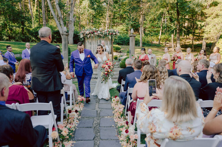 How do I explain the sincere and true feelings that Izzy and Brendan shared on their wedding day at one of the most magical place Arrow Park in Monroe NY. Izzy is Opera singer and Brendan is a Chef who owns his own restaurant called Circle in Newton, NJ got married at Arrow Park NY a month ago and it got real festive and wild real fast. But let's come back to the wild party in a bit and talk about their morning first. Izzy and Brendan both got ready onsite at Arrow Park, great thing about Arrow Park is that it has enough rooms to host all their bridal party and family. With all of Izzy and Brendan's loved ones onsite Izzy and Brendan's wedding prep was fun. No drama and no one running late, Izzy and Brendan's wedding prep went so smooth with everyone's cooperation! Izzy got into her dress with her mom and sister by her side, then we went down to the back steps for Izzy and Brendan's first look. Oh boy Brendan got super emotional for their first look, he couldn't even turn around to look at Izzy with all the happy emotions rushing to him. Izzy held his hand and they looked at each other. The two of them cried. Sharing such a beautiful first look Izzy and Brendan walked out to the front of Arrow Park for group and family photos. It was an August wedding so I kept everyone in the shade not too far, making it simple easy for group and family photos are important job to wedding photographer. After all the formal group photos were done, it was almost time for their wedding ceremony at the garden. Beautiful decor and floral arrangements were set up in the garden ready for Izzy and Brendan's wedding ceremony, guest started to walked down the long driveway and down the steps and found seats waited for the bride and groom to walk down the aisle. Brendan now standing in the front next to the priest, started tearing up as soon as he saw Izzy coming down the aisle escorted by her father. The two linked their eyes at each other and in the most loving way possible looked at each other through out the ceremony then sealed it with the first kiss as husband and wife. As calm and peaceful as Izzy and Brendan's wedding ceremony was, the two entered their reception each with (shaken) champagne bottles in their hands, everyone and anyone in Izzy and Brendan's way got sprayed with Champagne! They jumped, pouring Champagne into their friends mouth straight out of the bottle, then each drank some out of the bottle. Building the excitement in to their epic wedding party, Izzy and Brendan held each others hands and walked into the center of Arrow Park's courtyard and danced their first dance. Smoke and smell of freshly cooked dinner being prepared by Brendan's friends at Promises Kept Hudson Valley NY was filling the air, as first courses were being served. Happiest sound of plates, utensils and people chatting, Izzy and Brendan sat at their sweetheart table to enjoy their wedding dinner prepared by Promises Kept Hudson Valley NY. Then the evening got deeper and darker and vibe got stronger and crazier. Music got louder and everyone was in their element celebrating Izzy and Brendan on their wedding day. Izzy and Brendan's Arrow Park Monroe NY Wedding documented by by Karis | Hey Karis | Catskills, Hudson Valley NY elopement and wedding photographer | Brooklyn NY elopement and wedding photographer | Manhattan NY elopement and wedding photographer | Hey Karis is fun documentary wedding and elopement photographer.