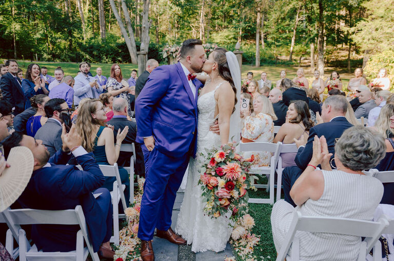 How do I explain the sincere and true feelings that Izzy and Brendan shared on their wedding day at one of the most magical place Arrow Park in Monroe NY. Izzy is Opera singer and Brendan is a Chef who owns his own restaurant called Circle in Newton, NJ got married at Arrow Park NY a month ago and it got real festive and wild real fast. But let's come back to the wild party in a bit and talk about their morning first. Izzy and Brendan both got ready onsite at Arrow Park, great thing about Arrow Park is that it has enough rooms to host all their bridal party and family. With all of Izzy and Brendan's loved ones onsite Izzy and Brendan's wedding prep was fun. No drama and no one running late, Izzy and Brendan's wedding prep went so smooth with everyone's cooperation! Izzy got into her dress with her mom and sister by her side, then we went down to the back steps for Izzy and Brendan's first look. Oh boy Brendan got super emotional for their first look, he couldn't even turn around to look at Izzy with all the happy emotions rushing to him. Izzy held his hand and they looked at each other. The two of them cried. Sharing such a beautiful first look Izzy and Brendan walked out to the front of Arrow Park for group and family photos. It was an August wedding so I kept everyone in the shade not too far, making it simple easy for group and family photos are important job to wedding photographer. After all the formal group photos were done, it was almost time for their wedding ceremony at the garden. Beautiful decor and floral arrangements were set up in the garden ready for Izzy and Brendan's wedding ceremony, guest started to walked down the long driveway and down the steps and found seats waited for the bride and groom to walk down the aisle. Brendan now standing in the front next to the priest, started tearing up as soon as he saw Izzy coming down the aisle escorted by her father. The two linked their eyes at each other and in the most loving way possible looked at each other through out the ceremony then sealed it with the first kiss as husband and wife. As calm and peaceful as Izzy and Brendan's wedding ceremony was, the two entered their reception each with (shaken) champagne bottles in their hands, everyone and anyone in Izzy and Brendan's way got sprayed with Champagne! They jumped, pouring Champagne into their friends mouth straight out of the bottle, then each drank some out of the bottle. Building the excitement in to their epic wedding party, Izzy and Brendan held each others hands and walked into the center of Arrow Park's courtyard and danced their first dance. Smoke and smell of freshly cooked dinner being prepared by Brendan's friends at Promises Kept Hudson Valley NY was filling the air, as first courses were being served. Happiest sound of plates, utensils and people chatting, Izzy and Brendan sat at their sweetheart table to enjoy their wedding dinner prepared by Promises Kept Hudson Valley NY. Then the evening got deeper and darker and vibe got stronger and crazier. Music got louder and everyone was in their element celebrating Izzy and Brendan on their wedding day. Izzy and Brendan's Arrow Park Monroe NY Wedding documented by by Karis | Hey Karis | Catskills, Hudson Valley NY elopement and wedding photographer | Brooklyn NY elopement and wedding photographer | Manhattan NY elopement and wedding photographer | Hey Karis is fun documentary wedding and elopement photographer.