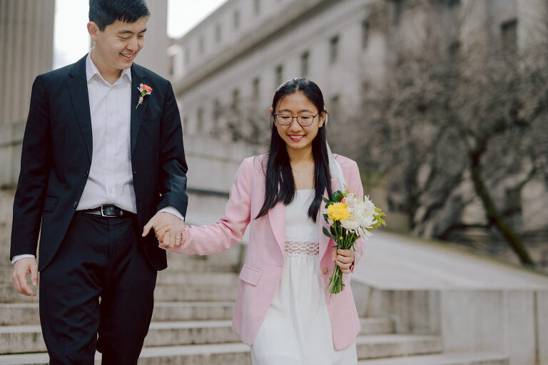 Alicia and Kevin made the bold decision to elope in the heart of the Big Apple before bidding adieu to city life and embracing suburban tranquility in New Jersey. Their choice resonates; after all, there's something undeniably magnetic about tying the knot in NYC that sets it apart from anywhere else in the world. Less than two weeks before their planned elopement at NYC City Hall, Alicia and Kevin reached out to me. I promptly scheduled a call to delve into the details, eager to understand their vision and expectations for their special day. It was essential for me to grasp their vibe and personalities; forging this connection and building relationship before the big day is super important to me. On April 5, I rendezvoused with Alicia and Kevin outside The Office of the City Clerk - Marriage Bureau. Despite hoping for a warm, sunny day, the brisk April air lingered, accompanied by a chilly breeze. Accompanied by a friend who served as their witness, we walked into the building. My camera was ready from outside documenting Alicia and Kevin, as I wanted to tell their story from beginning to end. Inside, we navigated the bureaucratic procedures, clicking away at Alicia and Kevin as they pleasantly waited for their number to be called. With paperwork signed and formalities concluded, Alicia and Kevin became husband and wife in the blink of an eye. We stayed a while longer inside the marriage bureau took the opportunity to capture some timeless moments posing on the iconic green sofa and NYC City Hall wall mural. Then we journeyed outside and wandered the vibrant bustling streets of NYC for some more photos. And what better way to conclude Alicia and Kevin's NYC City Hall elopement than with a quintessential New York slice. Alicia and Kevin NYC City Hall NY Elopement documented by by Karis | Hey Karis | Destination Wedding Photographer | Manhattan, Catskills, Hudson Valley, Brooklyn and NJ | Destination Elopement, Destination Wedding Photographer | Hey Karis is fun documentary wedding and elopement photographer based in NY, NJ.