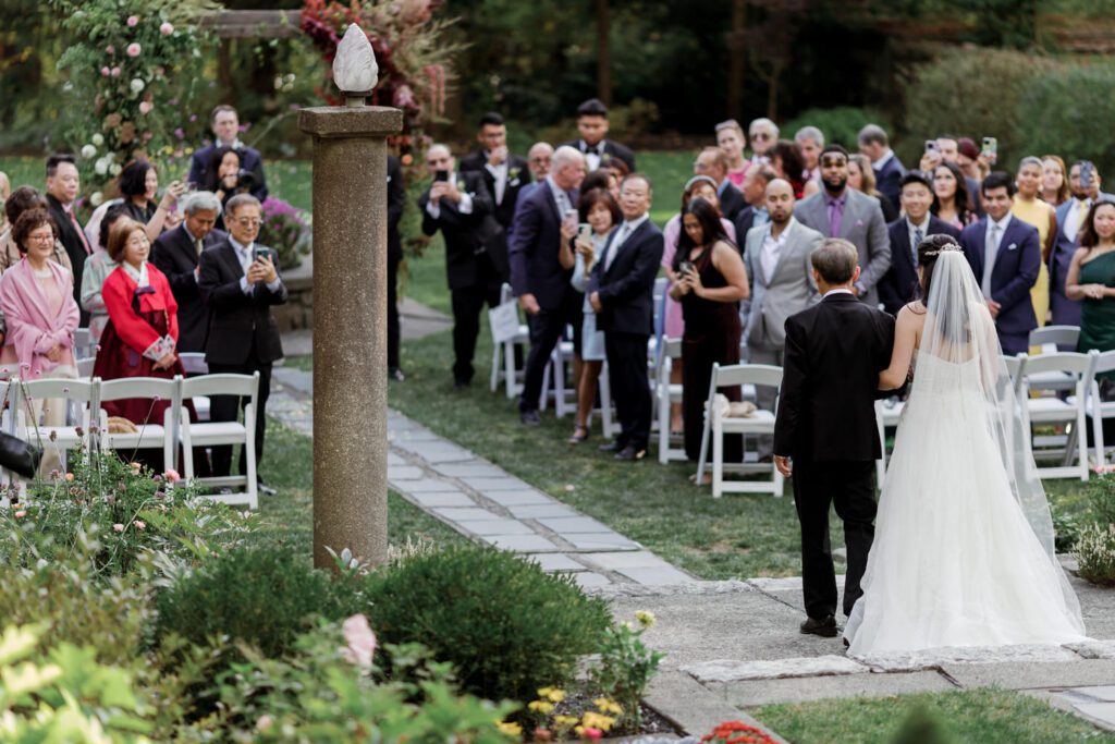 Vivian and Josh’s Gorgeous September Wedding at Arrow Park, NY
There’s something truly special about Arrow Park—it feels like my home away from home, and Vivian and Josh’s beautiful September wedding perfectly showcased everything this venue has to offer. Their blended celebration, honoring Vivian’s Korean heritage and Josh’s Jewish background, was a heartfelt and unforgettable day.
The couple beautifully wove their cultures into the festivities, from breaking the glass at the end of their garden ceremony to the lively horah during the reception. Later, Vivian and Josh delighted their guests by changing into traditional Korean hanbok outfits, a touching nod to her heritage.
Arrow Park: A Dream Venue for Multi-Day WeddingsVivian, Josh, and their loved ones all got ready at Arrow Park, which offers plenty of spacious accommodations for family and friends. This made it the perfect choice for their multi-day celebration. With its stunning grounds and versatile spaces, Arrow Park is ideal for couples seeking a wedding weekend filled with both elegance and comfort.
A Scenic September CelebrationThanks to the pleasant September weather, Vivian and Josh made full use of Arrow Park’s breathtaking grounds. Their day began with a magical first look along the iconic driveway lined with towering trees. From there, we explored the garden with its charming sculptures, captured moments by the ceremony’s floral décor, and took stunning portraits on the mansion’s iconic back staircase bathed in perfect lighting. We also ventured indoors for photos in the library and the Green Room, taking advantage of the mansion’s timeless charm.
As family and friends gathered, we captured formal portraits in front of the grand mansion before the ceremony began.
A Ceremony and Reception to RememberThe ceremony was set in the picturesque garden, where Jenny from Field Trip Flowers created a breathtaking floral backdrop that perfectly complemented the natural beauty of Arrow Park.
Afterward, guests strolled back to the mansion for a warm and inviting cocktail hour on the main floor. Later, everyone gathered in the courtyard for an enchanting outdoor reception under twinkling café lights. The space felt intimate yet grand, with the perfect blend of rustic elegance and romance.
Arrow Park’s charm, coupled with Vivian and Josh’s thoughtful cultural details, made this wedding one to remember. It’s the kind of venue where dreams come true—a hidden gem that’s ready to host your perfect day.
  
Thankful for all the wedding vendors that made this day possible:⁠
Venue: @arrowparkny
Floral: @fieldtripflowers
Catering: @lovenrosemary

Vivian and Josh Arrow Park NY Wedding documented by Karis from Hey Karis New York, Brooklyn, Hudson Valley NY and Catskills NY and NJ Wedding and NYC Elopement Photographer.