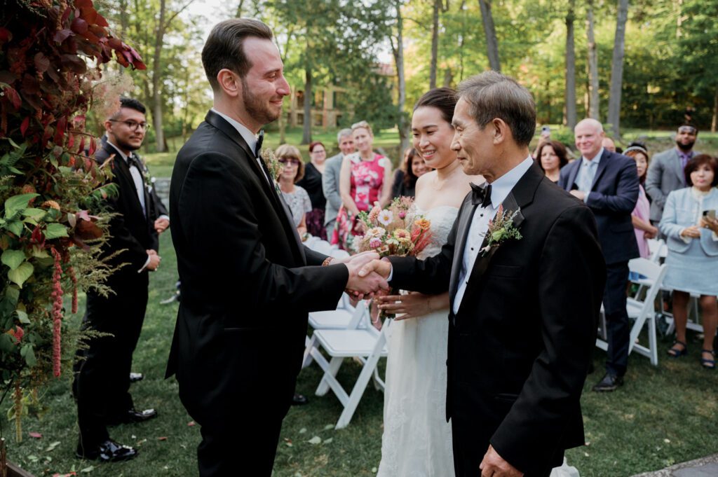 Vivian and Josh’s Gorgeous September Wedding at Arrow Park, NY
There’s something truly special about Arrow Park—it feels like my home away from home, and Vivian and Josh’s beautiful September wedding perfectly showcased everything this venue has to offer. Their blended celebration, honoring Vivian’s Korean heritage and Josh’s Jewish background, was a heartfelt and unforgettable day.
The couple beautifully wove their cultures into the festivities, from breaking the glass at the end of their garden ceremony to the lively horah during the reception. Later, Vivian and Josh delighted their guests by changing into traditional Korean hanbok outfits, a touching nod to her heritage.
Arrow Park: A Dream Venue for Multi-Day WeddingsVivian, Josh, and their loved ones all got ready at Arrow Park, which offers plenty of spacious accommodations for family and friends. This made it the perfect choice for their multi-day celebration. With its stunning grounds and versatile spaces, Arrow Park is ideal for couples seeking a wedding weekend filled with both elegance and comfort.
A Scenic September CelebrationThanks to the pleasant September weather, Vivian and Josh made full use of Arrow Park’s breathtaking grounds. Their day began with a magical first look along the iconic driveway lined with towering trees. From there, we explored the garden with its charming sculptures, captured moments by the ceremony’s floral décor, and took stunning portraits on the mansion’s iconic back staircase bathed in perfect lighting. We also ventured indoors for photos in the library and the Green Room, taking advantage of the mansion’s timeless charm.
As family and friends gathered, we captured formal portraits in front of the grand mansion before the ceremony began.
A Ceremony and Reception to RememberThe ceremony was set in the picturesque garden, where Jenny from Field Trip Flowers created a breathtaking floral backdrop that perfectly complemented the natural beauty of Arrow Park.
Afterward, guests strolled back to the mansion for a warm and inviting cocktail hour on the main floor. Later, everyone gathered in the courtyard for an enchanting outdoor reception under twinkling café lights. The space felt intimate yet grand, with the perfect blend of rustic elegance and romance.
Arrow Park’s charm, coupled with Vivian and Josh’s thoughtful cultural details, made this wedding one to remember. It’s the kind of venue where dreams come true—a hidden gem that’s ready to host your perfect day.
  
Thankful for all the wedding vendors that made this day possible:⁠
Venue: @arrowparkny
Floral: @fieldtripflowers
Catering: @lovenrosemary

Vivian and Josh Arrow Park NY Wedding documented by Karis from Hey Karis New York, Brooklyn, Hudson Valley NY and Catskills NY and NJ Wedding and NYC Elopement Photographer.