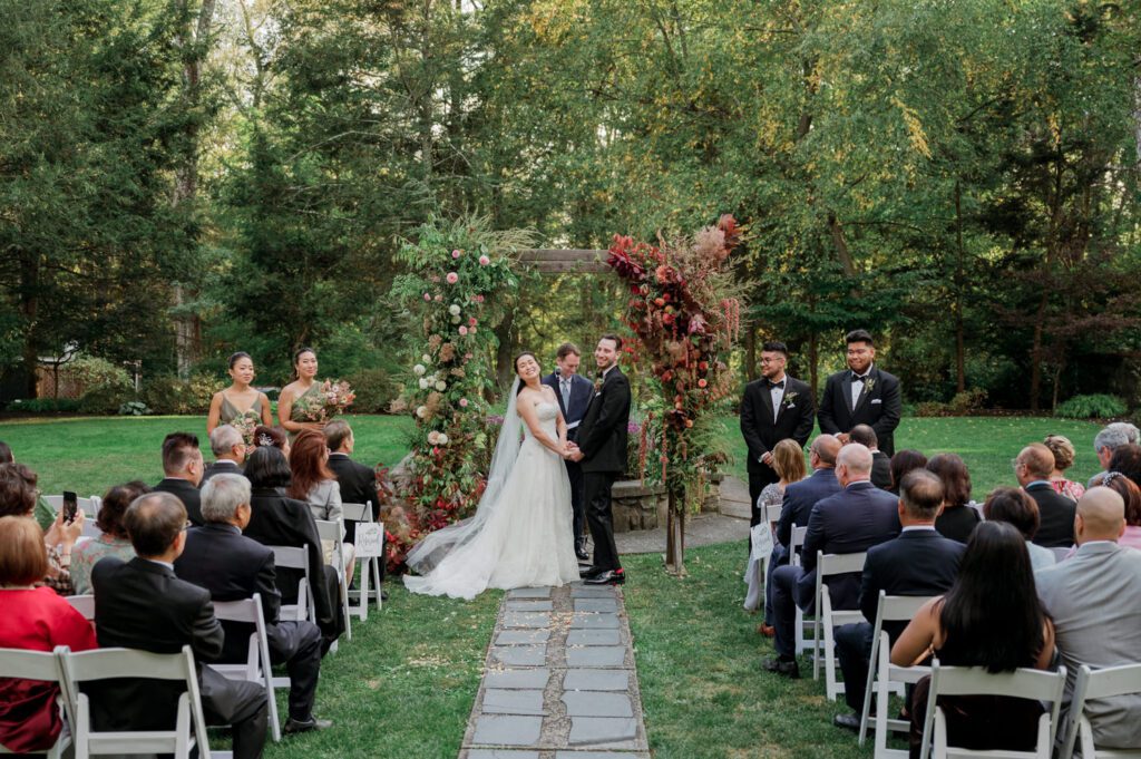 Vivian and Josh’s Gorgeous September Wedding at Arrow Park, NY
There’s something truly special about Arrow Park—it feels like my home away from home, and Vivian and Josh’s beautiful September wedding perfectly showcased everything this venue has to offer. Their blended celebration, honoring Vivian’s Korean heritage and Josh’s Jewish background, was a heartfelt and unforgettable day.
The couple beautifully wove their cultures into the festivities, from breaking the glass at the end of their garden ceremony to the lively horah during the reception. Later, Vivian and Josh delighted their guests by changing into traditional Korean hanbok outfits, a touching nod to her heritage.
Arrow Park: A Dream Venue for Multi-Day WeddingsVivian, Josh, and their loved ones all got ready at Arrow Park, which offers plenty of spacious accommodations for family and friends. This made it the perfect choice for their multi-day celebration. With its stunning grounds and versatile spaces, Arrow Park is ideal for couples seeking a wedding weekend filled with both elegance and comfort.
A Scenic September CelebrationThanks to the pleasant September weather, Vivian and Josh made full use of Arrow Park’s breathtaking grounds. Their day began with a magical first look along the iconic driveway lined with towering trees. From there, we explored the garden with its charming sculptures, captured moments by the ceremony’s floral décor, and took stunning portraits on the mansion’s iconic back staircase bathed in perfect lighting. We also ventured indoors for photos in the library and the Green Room, taking advantage of the mansion’s timeless charm.
As family and friends gathered, we captured formal portraits in front of the grand mansion before the ceremony began.
A Ceremony and Reception to RememberThe ceremony was set in the picturesque garden, where Jenny from Field Trip Flowers created a breathtaking floral backdrop that perfectly complemented the natural beauty of Arrow Park.
Afterward, guests strolled back to the mansion for a warm and inviting cocktail hour on the main floor. Later, everyone gathered in the courtyard for an enchanting outdoor reception under twinkling café lights. The space felt intimate yet grand, with the perfect blend of rustic elegance and romance.
Arrow Park’s charm, coupled with Vivian and Josh’s thoughtful cultural details, made this wedding one to remember. It’s the kind of venue where dreams come true—a hidden gem that’s ready to host your perfect day.
  
Thankful for all the wedding vendors that made this day possible:⁠
Venue: @arrowparkny
Floral: @fieldtripflowers
Catering: @lovenrosemary

Vivian and Josh Arrow Park NY Wedding documented by Karis from Hey Karis New York, Brooklyn, Hudson Valley NY and Catskills NY and NJ Wedding and NYC Elopement Photographer.